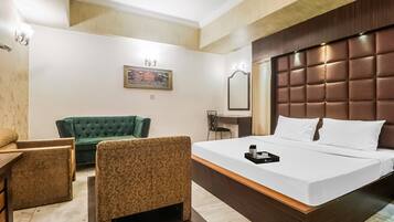 A hotel room with a large bed, a green sofa, a small table, and a mirror.
