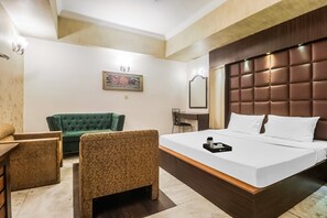 A hotel room with a large bed, a green sofa, a small table, and a mirror. - Townhouse Hotel Taksonz (Ludhiana)