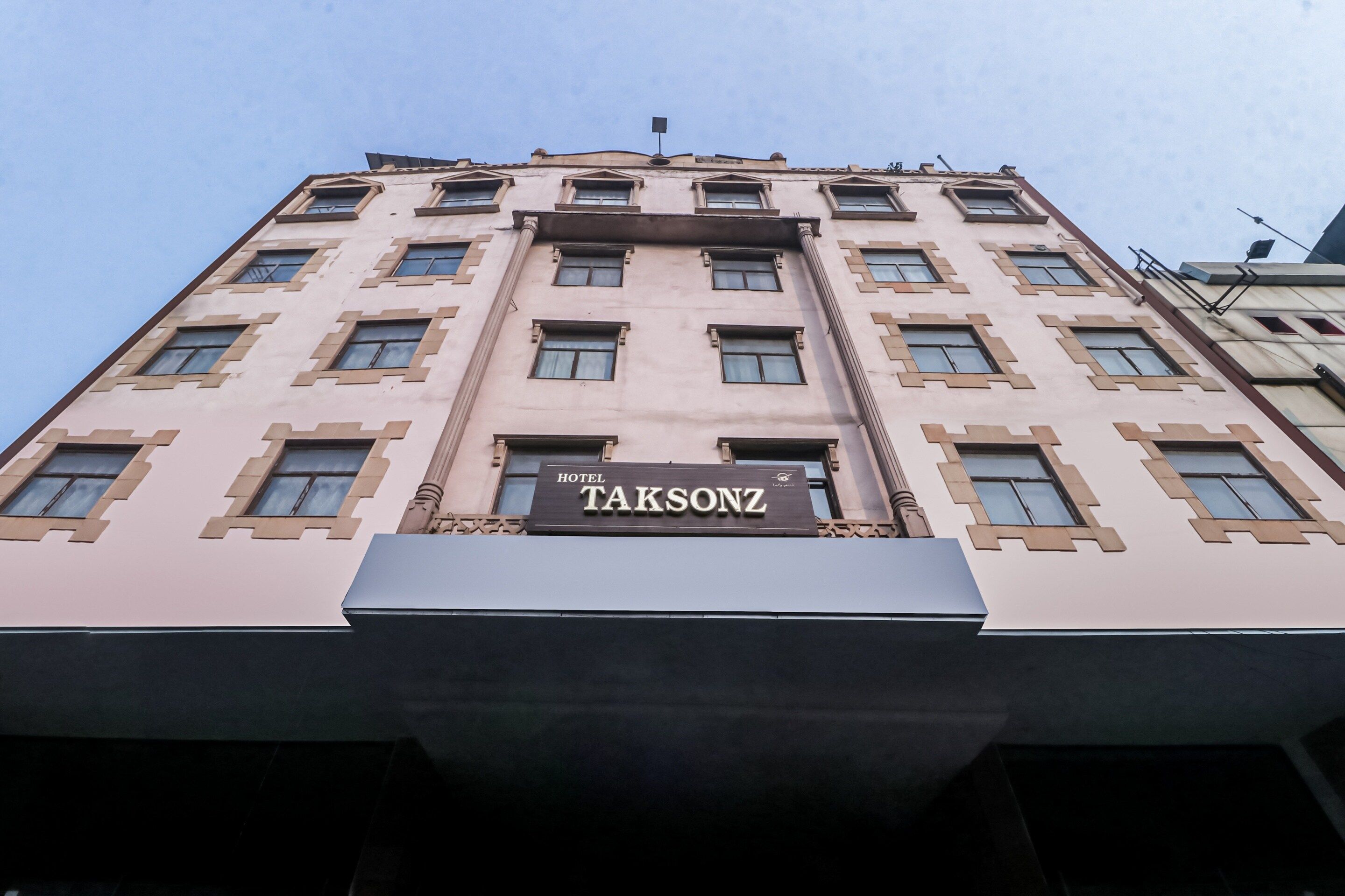 Un edificio de varios pisos con un letrero llamativo que dice 'HOTEL TAKSONZ' al nivel de la calle.