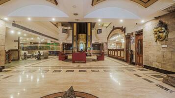 A spacious lobby with a central reception desk, a Buddha statue, and a marble floor with geometric patterns.