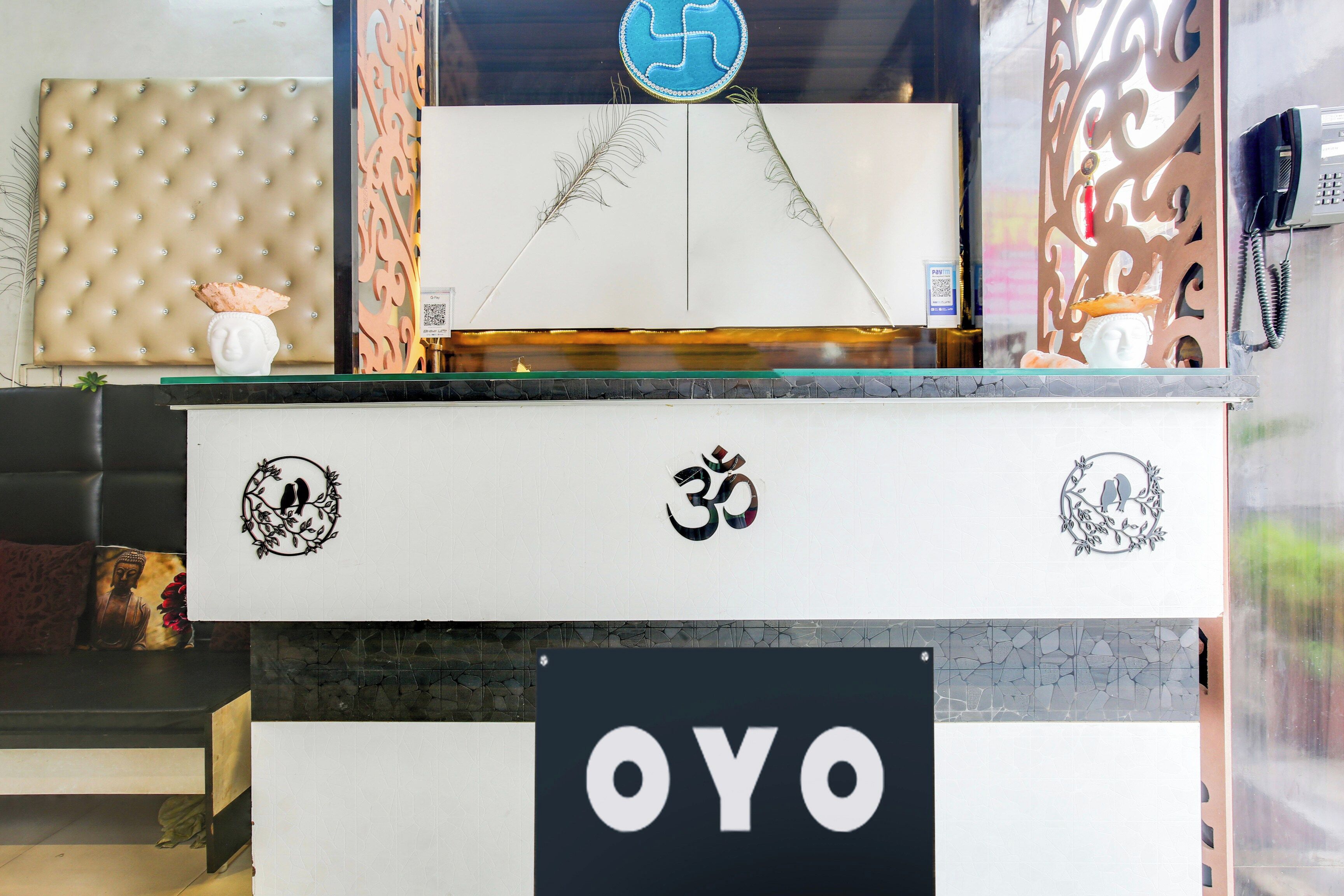 A reception desk with a sign reading 'OYO' and decorative elements including a Buddha statue, a bird motif, and a 'Pay Here' machine.