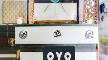 A reception desk with a sign reading 'OYO' and decorative elements including a Buddha statue, a bird motif, and a 'Pay Here' machine.