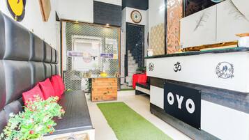 A modern interior with a check-in counter, a sofa with red cushions, and a decorative plant.