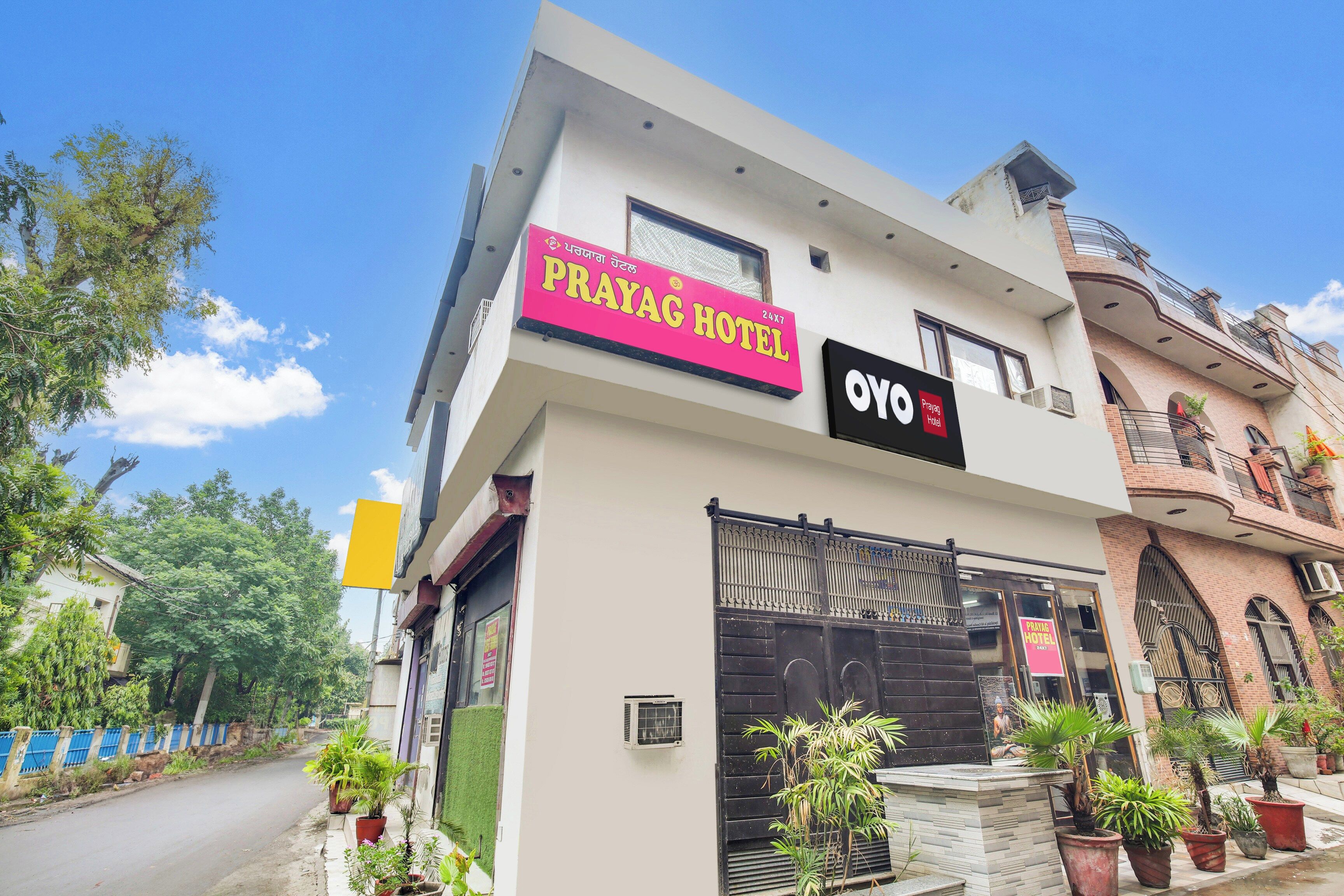 A hotel named 'Prayag Hotel' with a modern facade, a prominent sign, and a gated entrance.