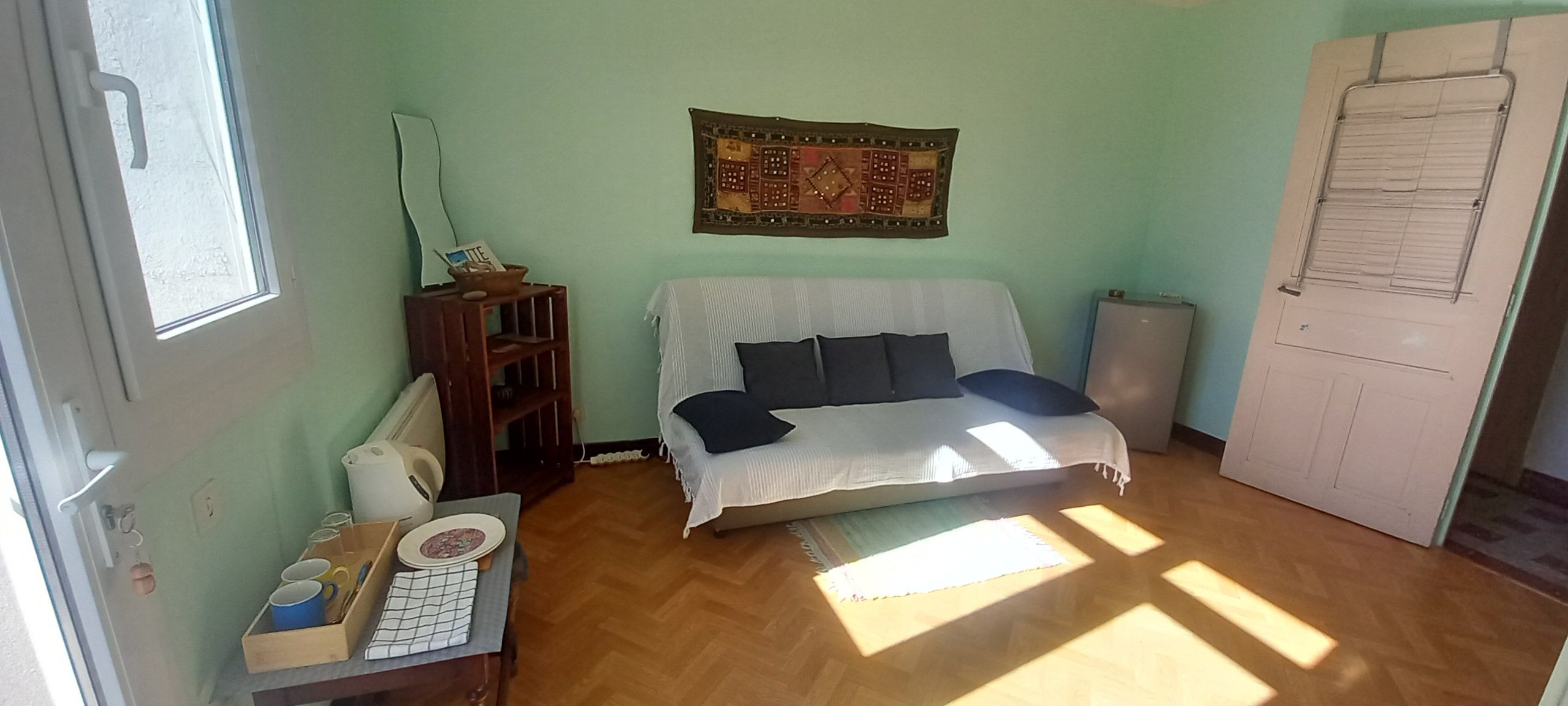 Une pièce comprenant un lit, une petite table avec quelques ustensiles de cuisine, un radiateur et une porte avec une fenêtre.
