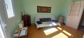 Una habitació amb un llit, una taula petita amb utensilis de cuina, un radiador i una porta amb finestral.
