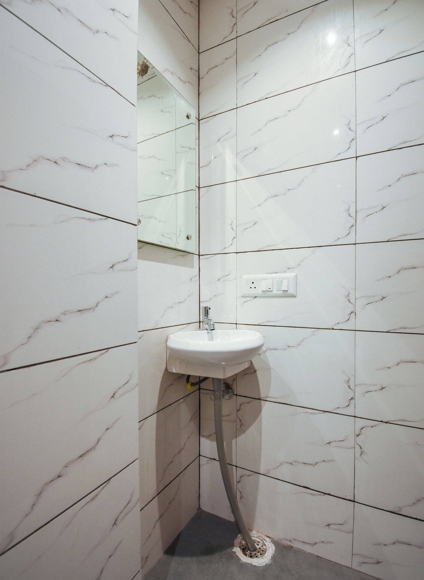 Une salle de bain avec des carreaux de marbre blanc, un lavabo blanc et un miroir.