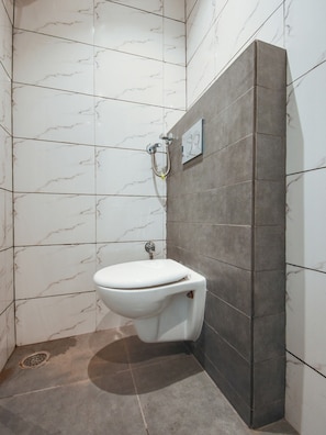 A bathroom with a toilet, a shower, and a wall-mounted mirror. - HOTEL O G S HOME (Ludhiana)