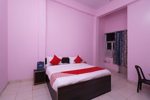 A bedroom with a bed, pillows, a nightstand, a chair, and a window with curtains. - Hotel O Capital Inn (Lucknow)