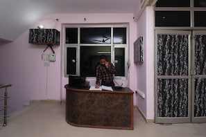 A reception desk with a person standing behind it, a window with a view of the sky, and a door with a patterned curtain. - Hotel O Capital Inn (Lucknow)