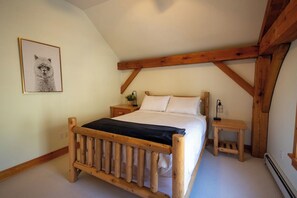 Een slaapkamer met een houten bedframe, wit beddengoed, een nachtkastje met een lamp en een lijst met een foto aan de muur.