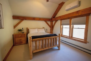 Une chambre à coucher avec un lit en bois, une table de chevet, une fenêtre avec des stores et un appareil de climatisation.