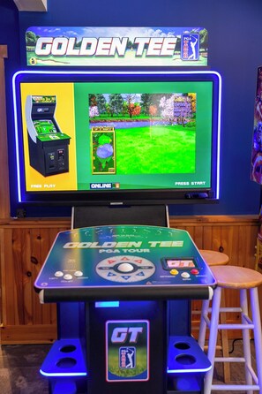 Een videospelconsole met een scherm waarop een golfspel wordt weergegeven, een krukje en een tv die aan de muur is bevestigd.
