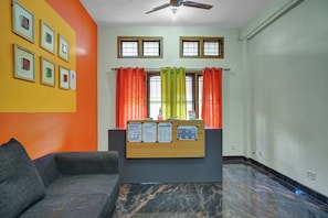 A room with a grey sofa, a wooden information board, and a window with orange and green curtains. - Collection O Lala Homes (Kochi)