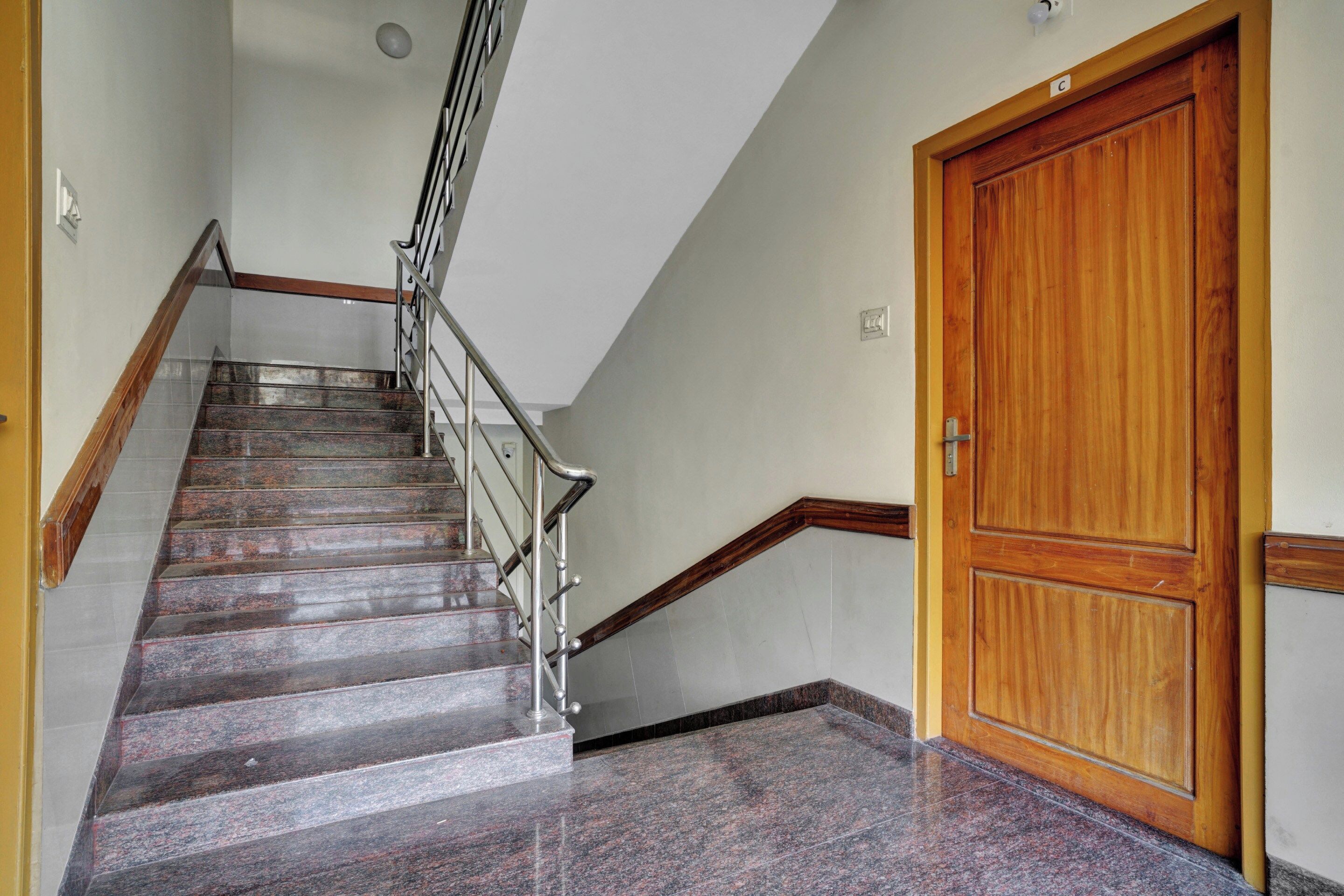 Un escalier avec une rampe métallique, une porte en bois et un sol carrelé.