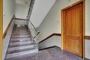 A staircase with a metal handrail, a wooden door, and a tiled floor. - Collection O Lala Homes (Aluva)