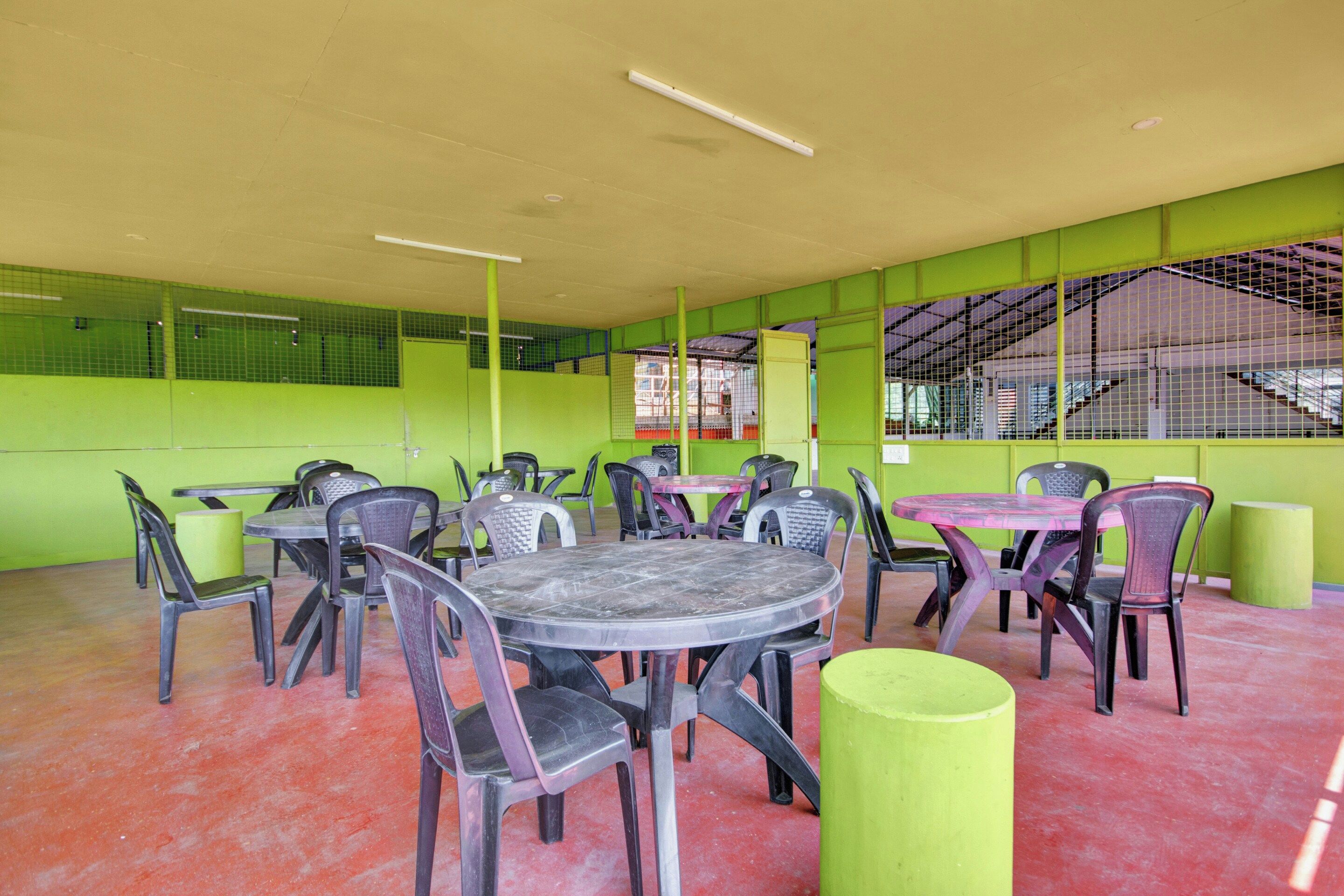 A dining area with round tables and chairs, green walls, and a high ceiling.