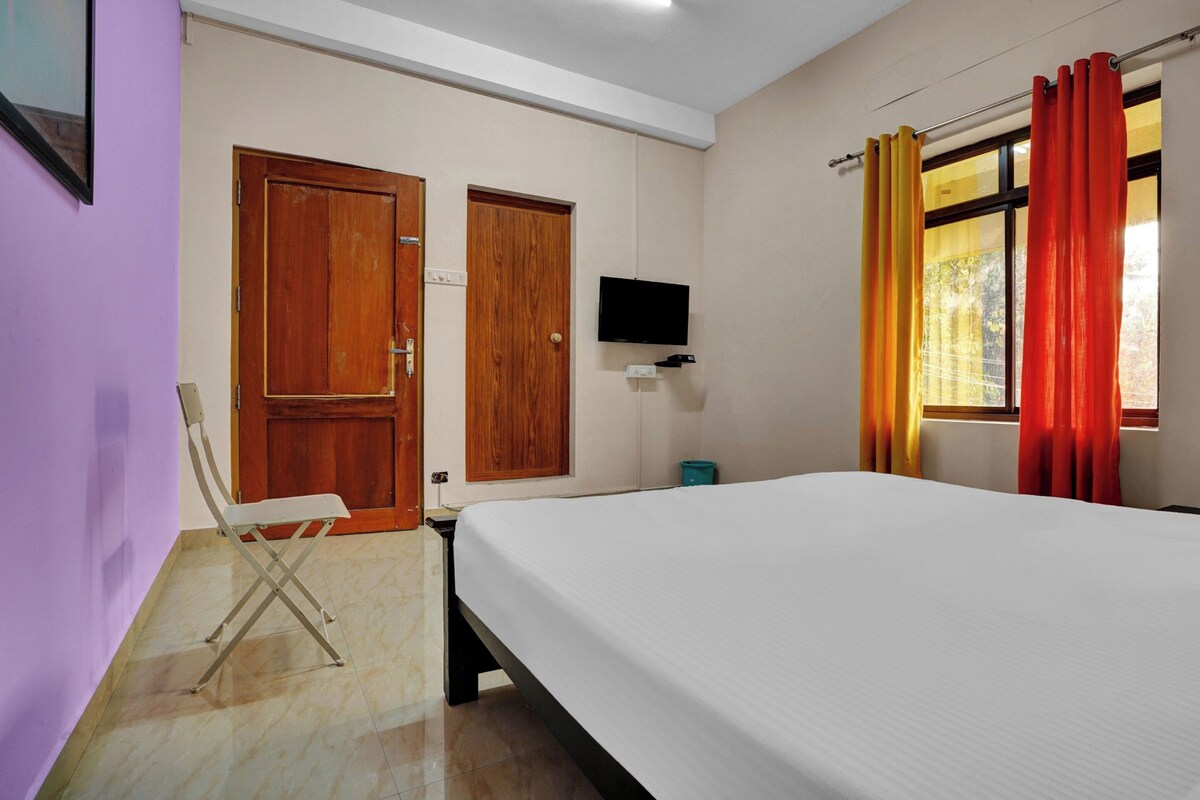 Un dormitorio con cama, televisión en la pared y ventana con cortinas.