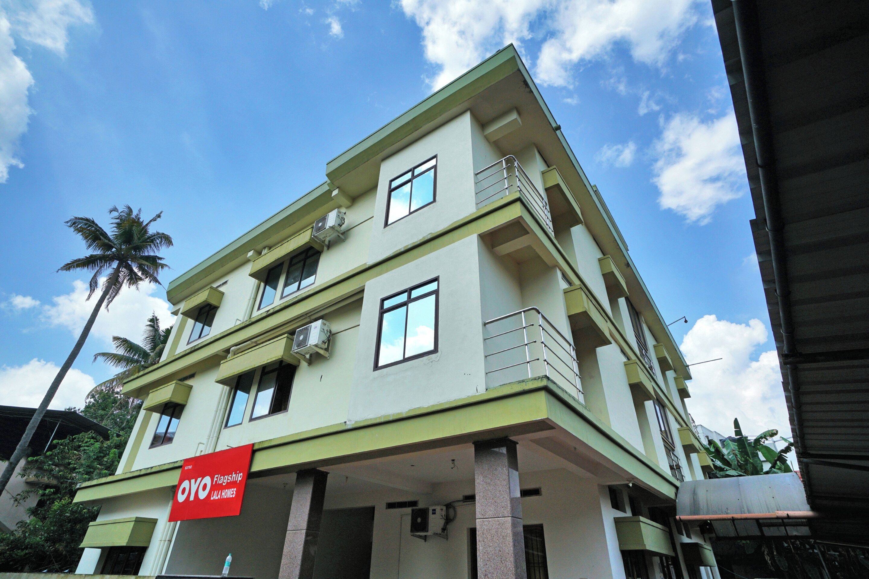 A multi-story building with balconies and air conditioning units, featuring a prominent red sign for OYO Flagship Lala Homes.