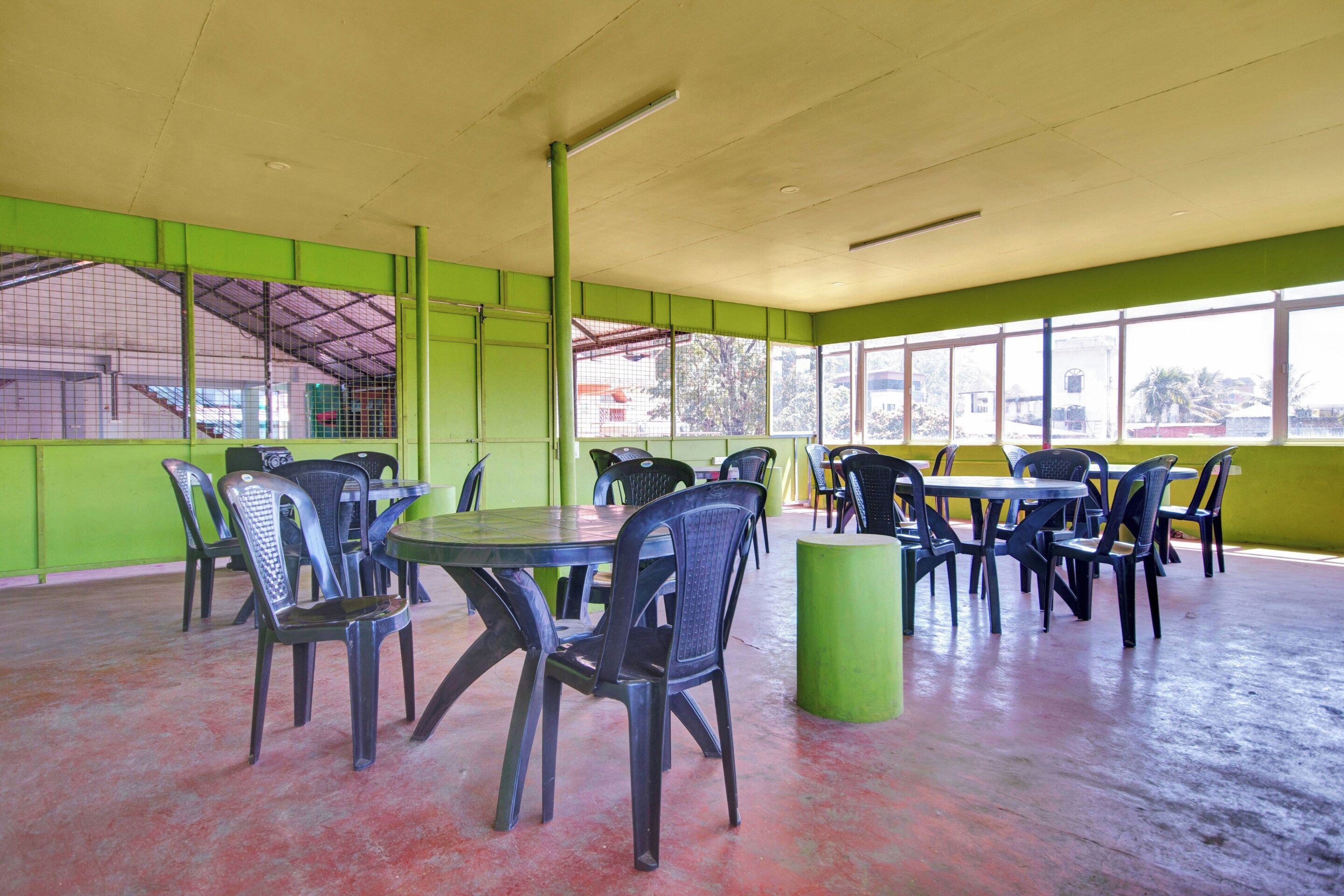 A spacious indoor area with multiple tables and chairs, large windows, and a green wall.