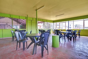 A spacious indoor area with multiple tables and chairs, large windows, and a green wall. - Collection O Lala Homes (Kochi)
