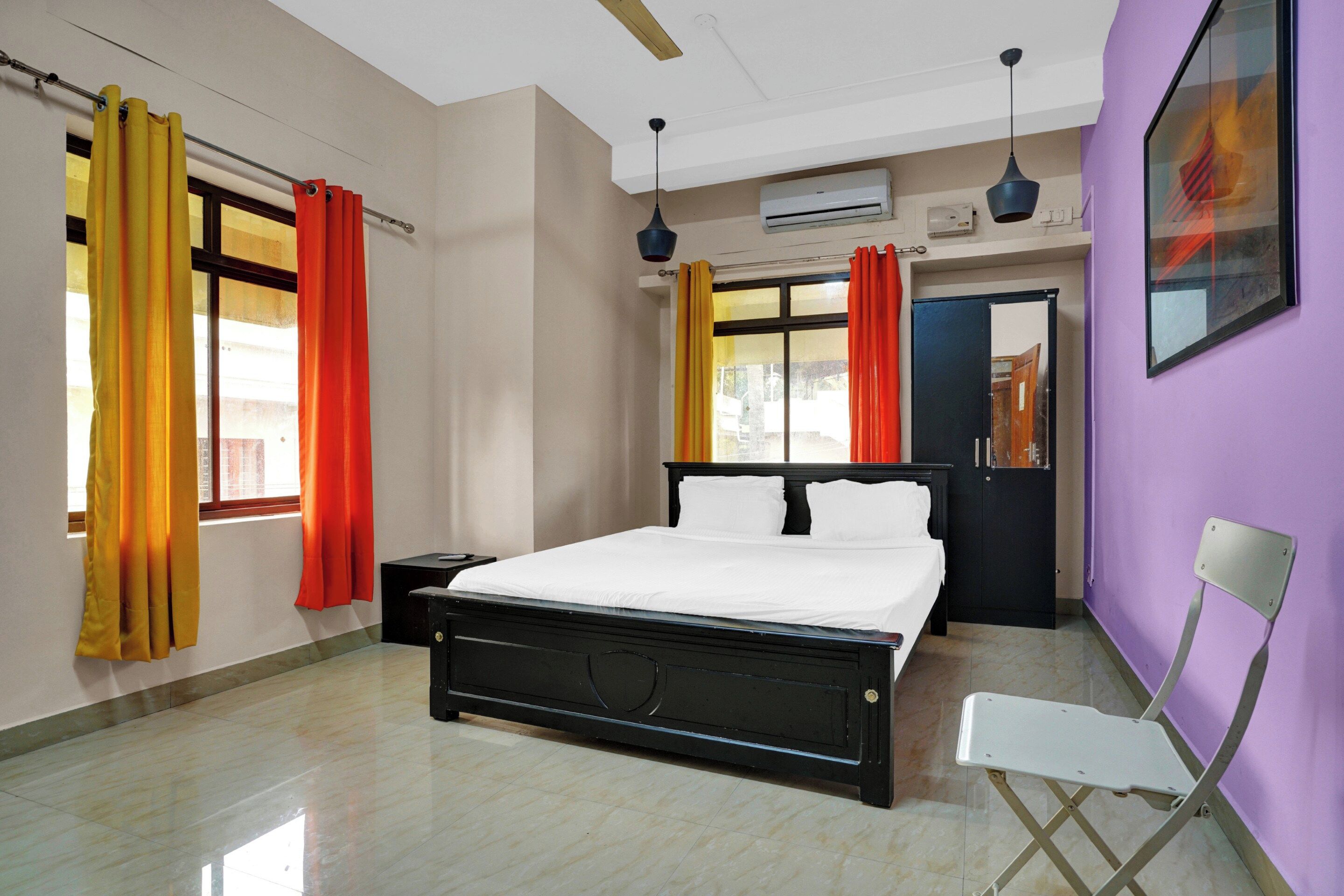 Una habitación de hotel con cama, mesita de noche, silla, armario y ventana con cortinas.