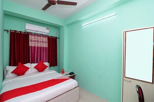 Habitación de hotel con cama, cortinas rojas, ventilador de techo, unidad de aire acondicionado, teléfono junto a la cama y una puerta con espejo.