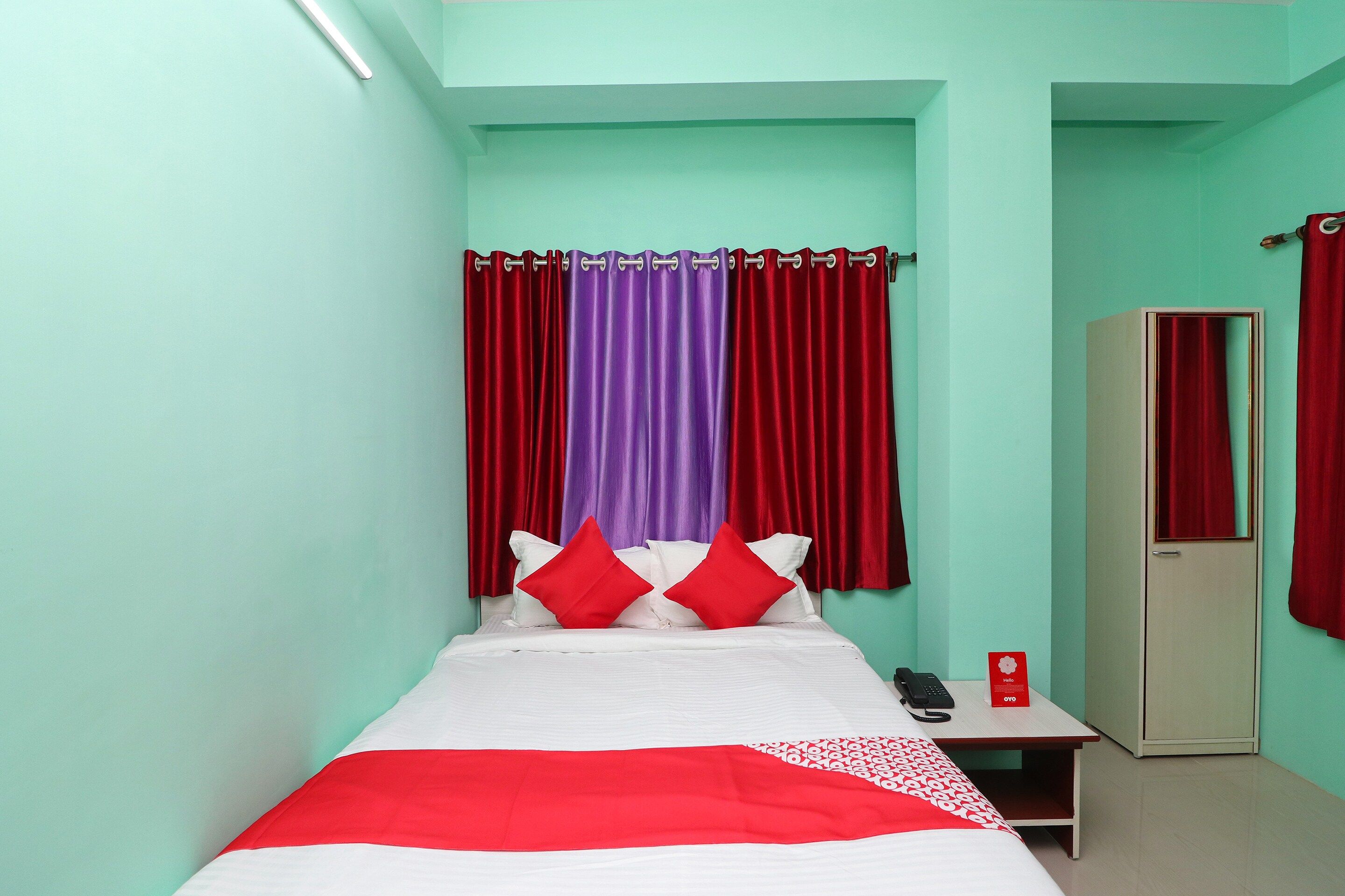 A single bed with a red and white bedspread, two red pillows, and a telephone on a bedside table.