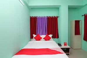 Un letto singolo con copriletto rosso e bianco, due cuscini rossi e un telefono su un comodino.