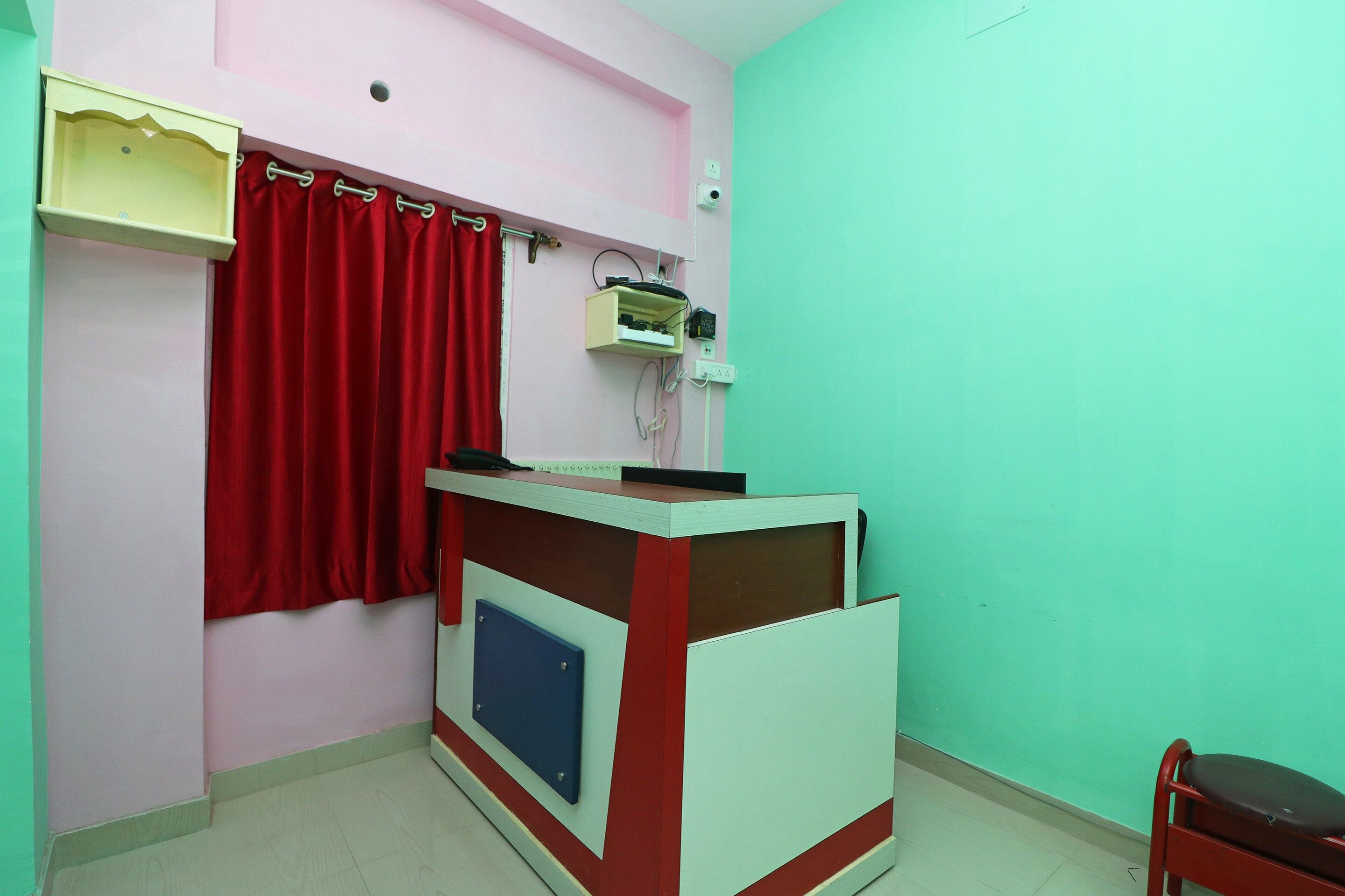 A small, brightly colored room with a reception desk, a red curtain, and a chair.