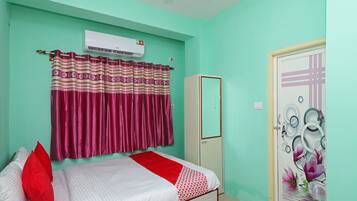 A room with a bed, a wardrobe, a door with a decorative plate, and an air conditioning unit.