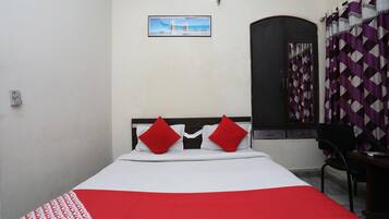 A bed with a white and red bedspread, two red pillows, and a picture of a bridge on the wall.