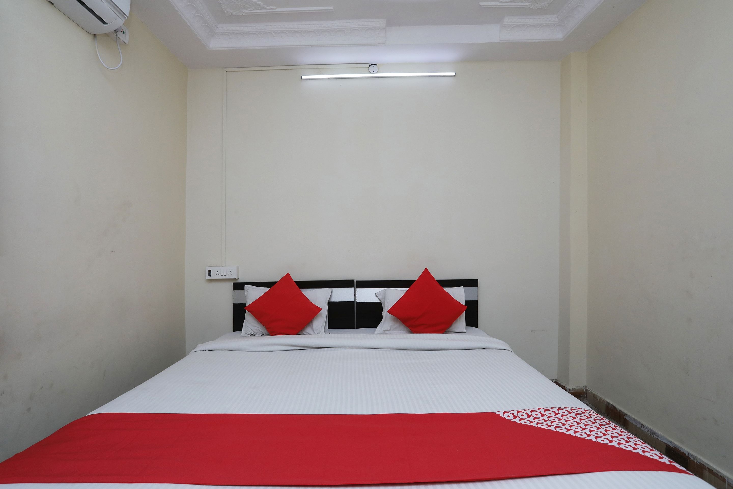 Una cama individual con colcha blanca y roja, dos almohadas rojas y un cabecero negro y blanco.