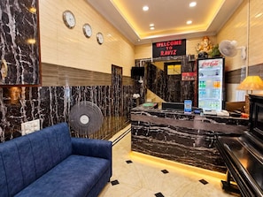 A hotel lobby with a reception desk, a blue sofa, a Coca-Cola refrigerator, and a wall clock. - Hotel O Raviz Inn (Kolkata)