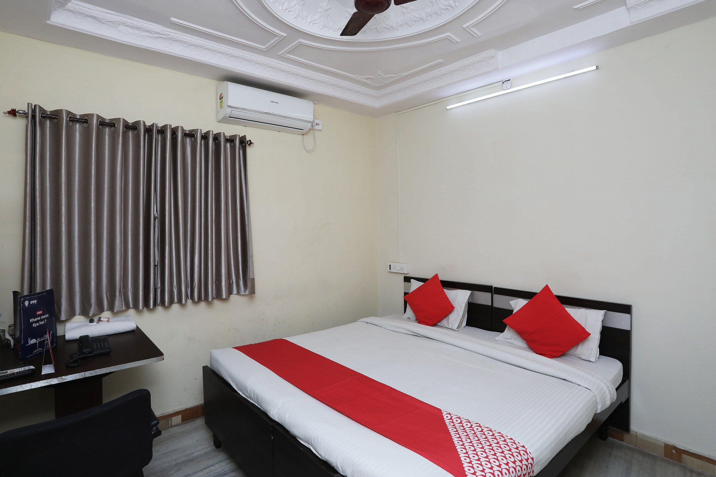 A hotel room with a bed, a desk, a chair, an air conditioner, and a ceiling fan.