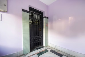 Um corredor com um portão de metal preto, uma porta verde e piso de azulejos.
