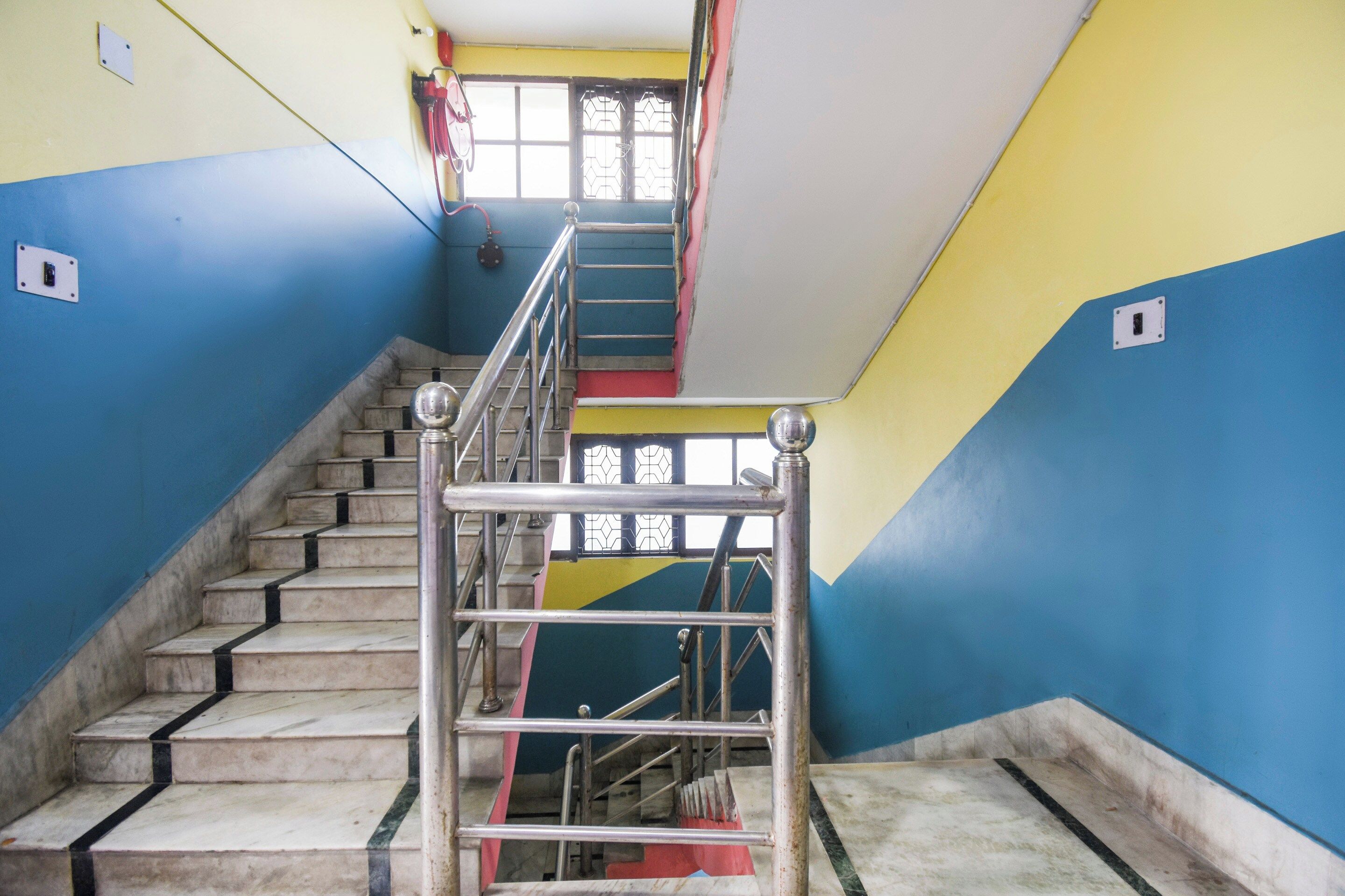 Un escalier avec des rampes en métal et des marches en marbre, menant à un palier doté d’une fenêtre.