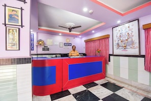 Bancada de recepção com ventilador de teto, relógio e pôster religioso emoldurado.