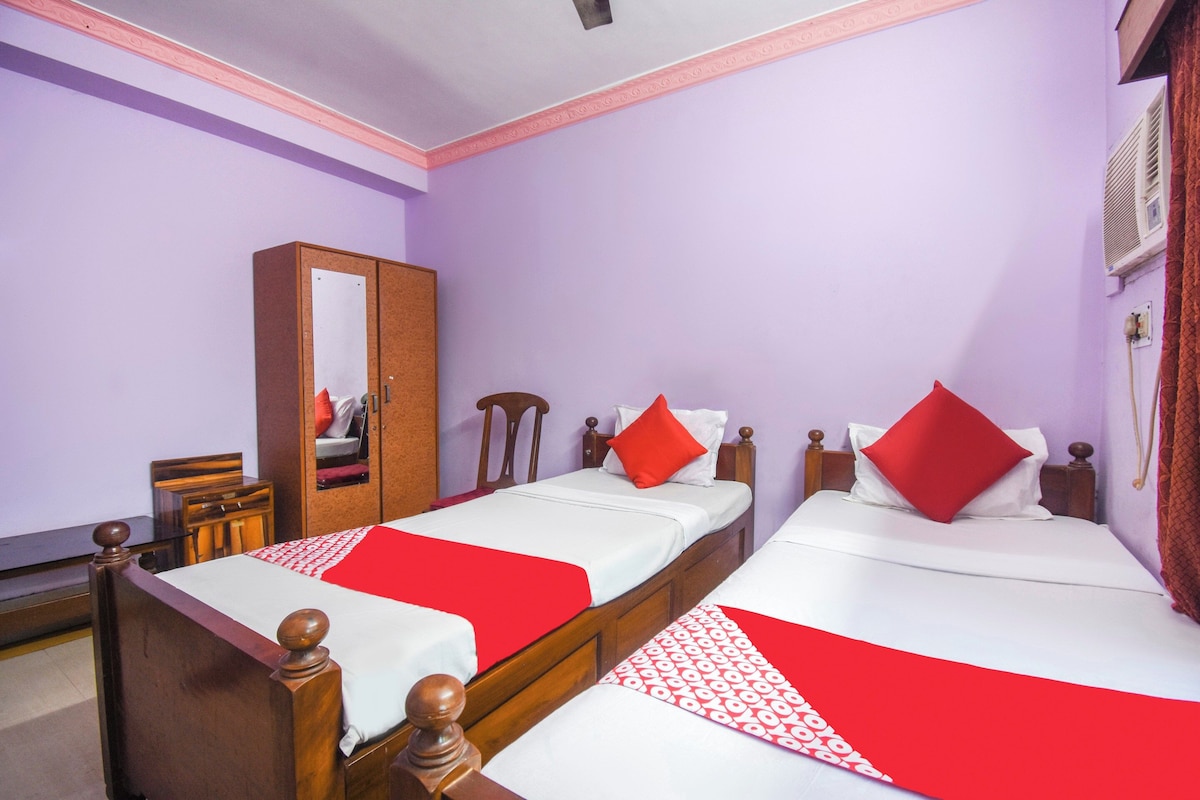 Una habitación de hotel con dos camas individuales, un armario de madera, un espejo y una colcha estampada en rojo y blanco.
