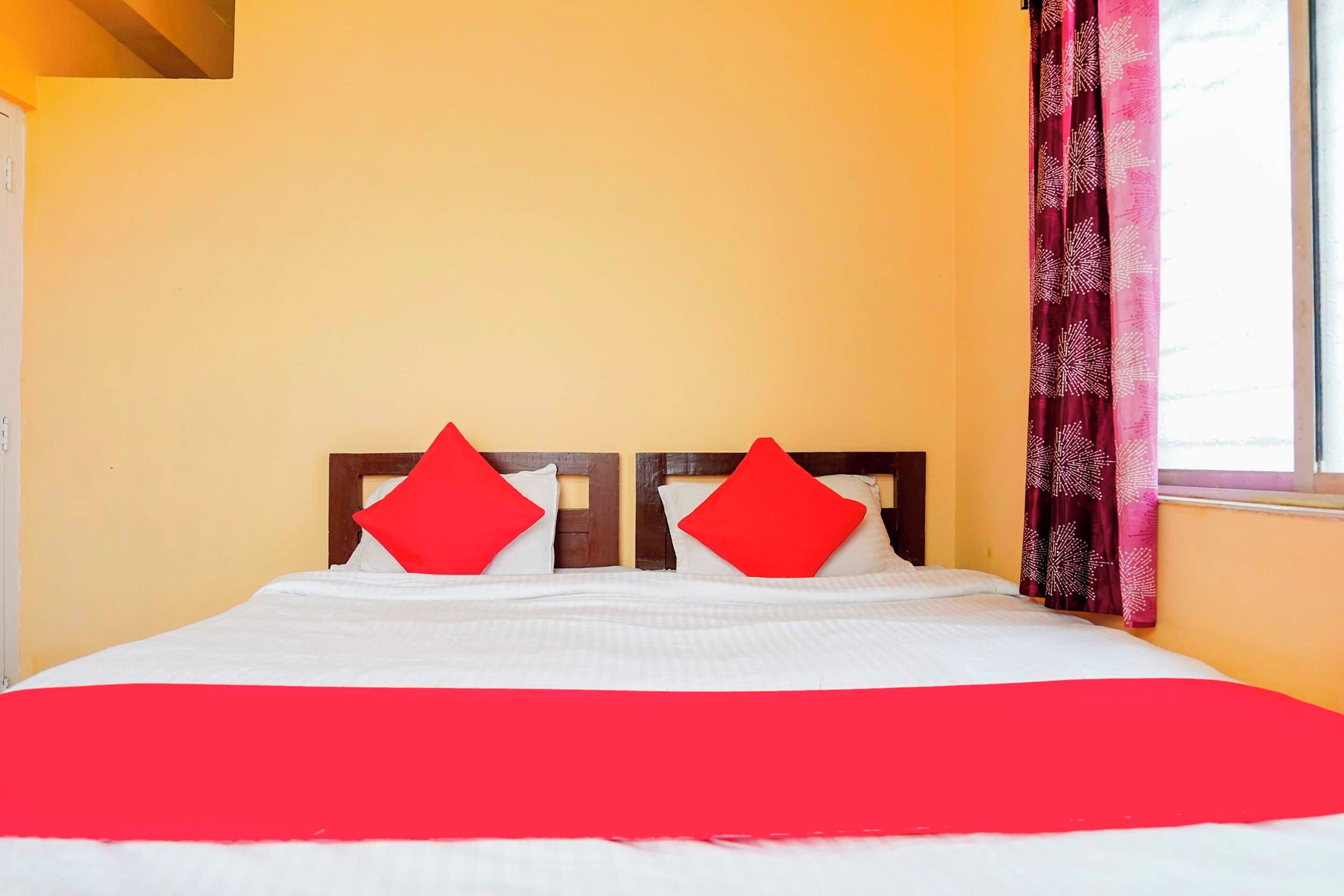 A bed with white bedding and two red pillows, a window with curtains, and a yellow wall.