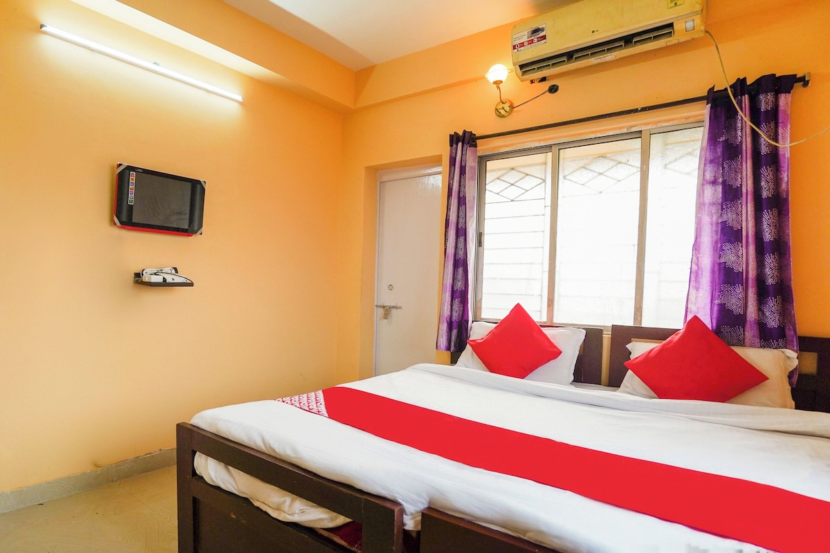 A hotel room with a bed, a television on the wall, and an air conditioning unit.