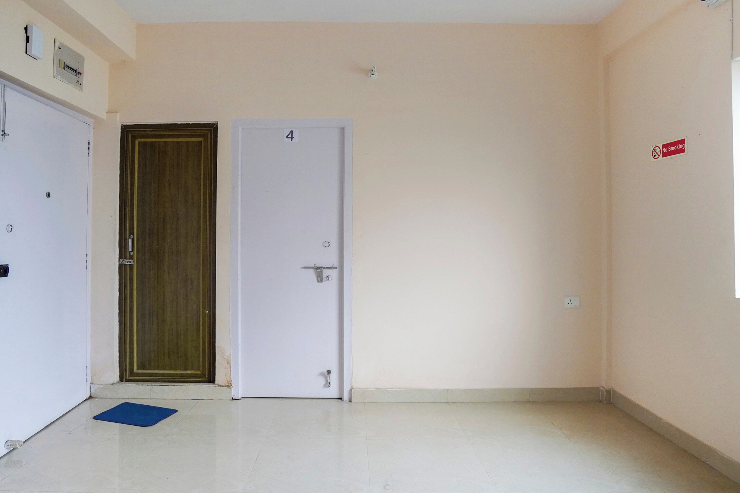 A hallway with a closed door, a blue mat on the floor, and a 'No Smoking' sign on the wall.