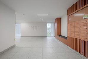 A clean, modern hallway with a tiled floor, a wall-mounted directory, and a bench. - Lumina 2-room Apt w/ Parking I Balcony (Warszawa)