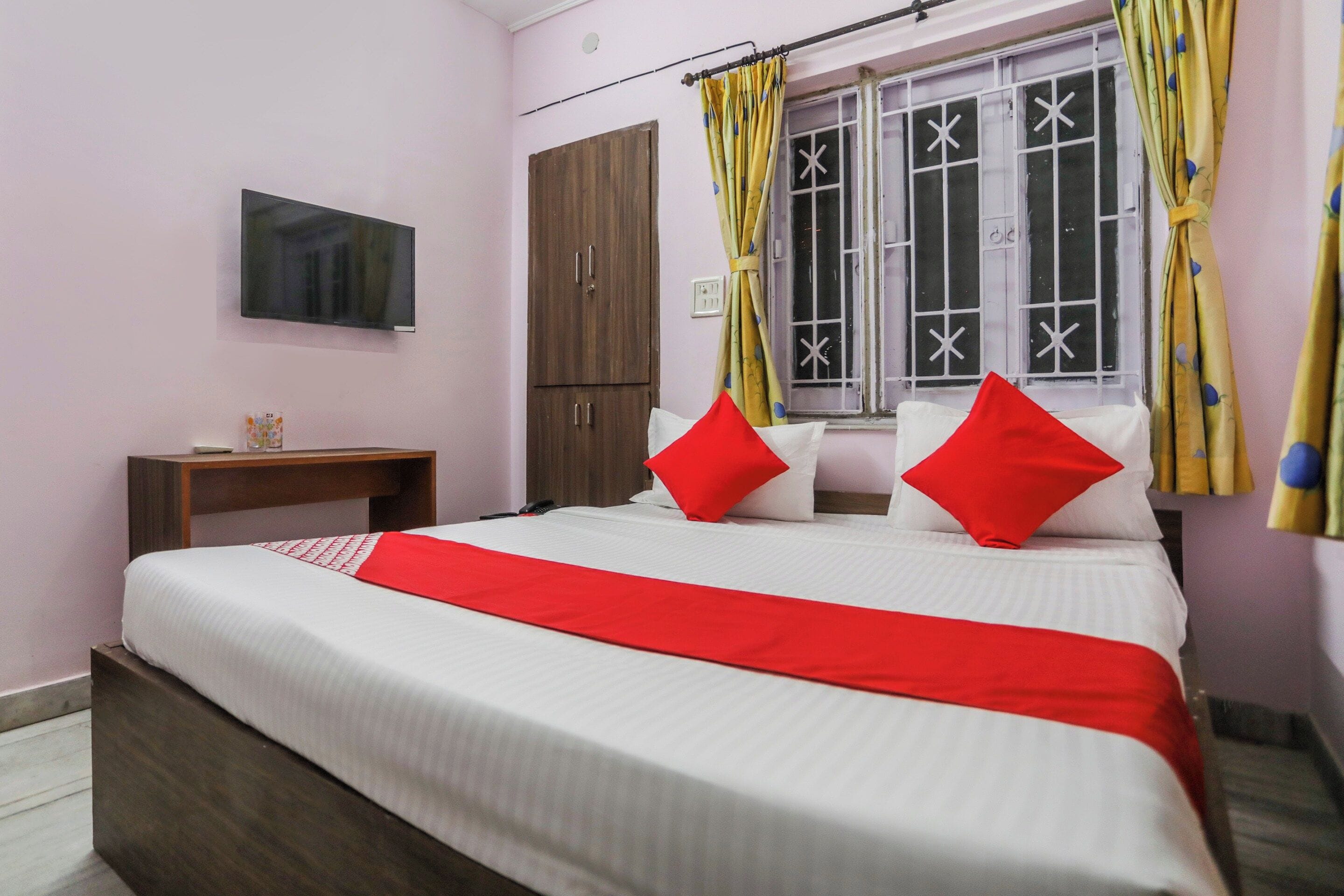 Habitación de hotel con cama, televisión, armario, mesita de noche y ventana con cortinas.