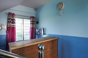 Ein Zimmer mit einem Holztisch, einem Vorhangfenster, einem Wandventilator und einer Überwachungskamera.