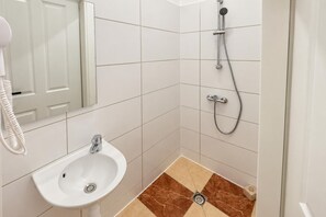 Un bagno con un lavandino bianco, uno specchio e una doccia dotata di soffione manuale.