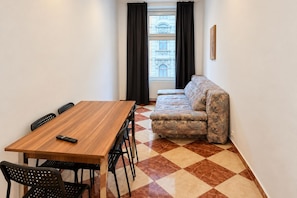 A dining area with a wooden table and chairs, a sofa, and a window with curtains. - Six Tickets to Vienna 2BR near Westbahnhof (Vienna)