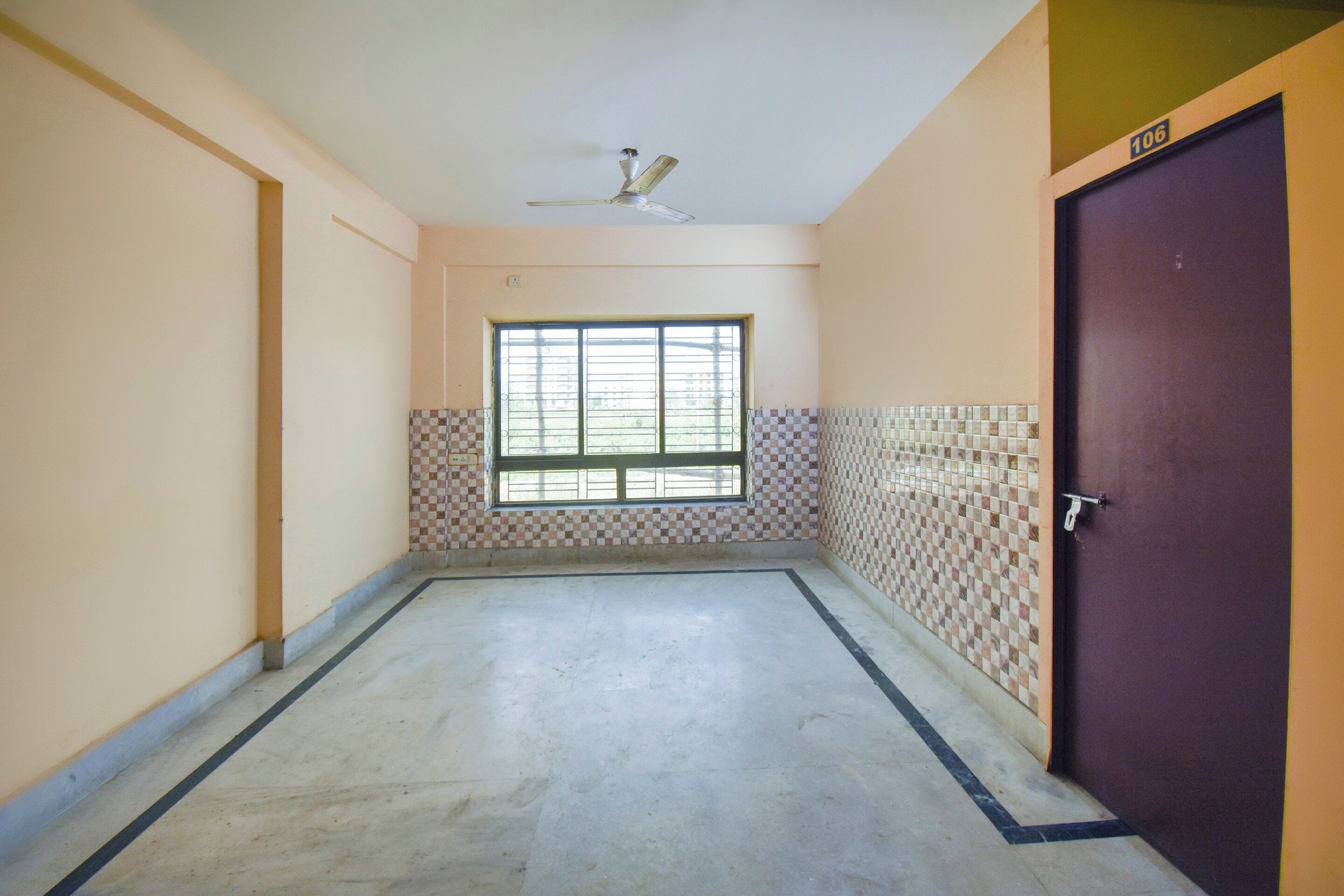 A corridor with a window, tiled walls, a ceiling fan, and a door.