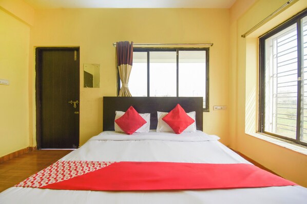 A hotel room with a bed, a window, a door, and a mirror.