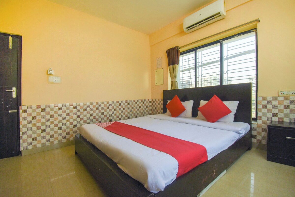 A hotel room with a bed, a nightstand, a window with curtains, an air conditioning unit, and a tiled wall.